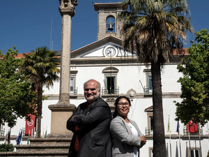 Un hombre y una mujer posan frente a un edificio blanco que tiene una campana en la parte superior