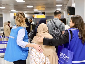 Dos mujeres que llevan puestos chalecos azules acompañan a una mujer que lleva un velo en su cabeza en un aeropuerto.