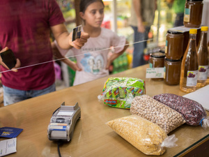 Un hombre está por pagar una compra en una tienda de conveniencia con una tarjeta; junto a él, su pequeña hija.