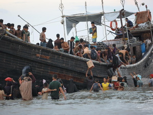 Decenas de personas se ven a bordo de una destartalada embaracación y de pie en las aguas bajas que la rodean, algunos ayudando a otros a bajarse del barco, otros más descargando bultos y cajas.