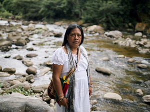 Una mujer de cabello oscuro vestida de blanco junto a un río.