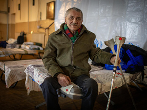 Sentado en una cama en un centro de tránsito, un hombre ucraniano de 59 años mira fijamente a la cámara; con la mano izquierda sostiene un par de muletas.