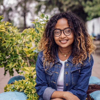 Una chica de lentes y cabello rizado sonría a la cámara