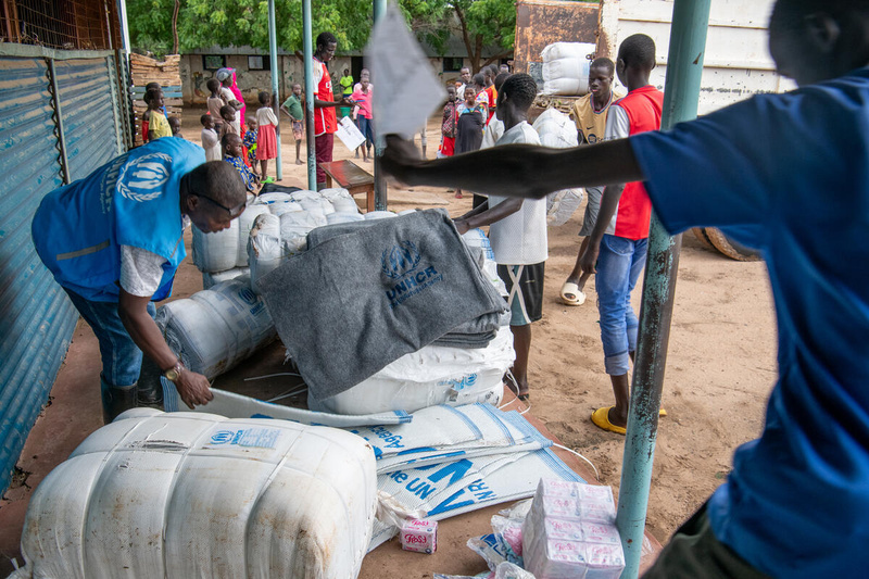 Un miembro del personal de ACNUR entrega láminas de plástico y mantas a la población refugiada afectada por las inundaciones