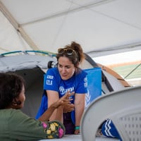 Una mujer con camisa de ACNUR habla con otra mujer en un campamento transitorio.