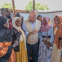 Un grupo de mujeres y hombres, con el Alto Comisionado de las Naciones Unidas para los Refugiados, Barham Salih, en el centro, conversa sonriendo. 