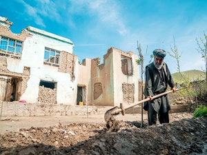 Un hombre cava una zanja para un árbol frente a las ruinas de una casa bombardeada.