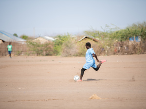 Una niña se prepara para patear un balón en un campo cubierto de polvo.