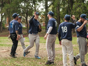 Seis hombres con uniforme deportivo color azul marino y gris en un campo de juego, al fondo árboles