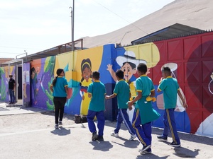 Cuatro niños y una niña caminan al lado de un mural colorido en una escuela