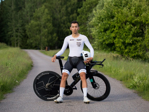 Un hombre con ropa deportiva posa junto a su bicicleta mientras sostiene un caso con su mano izquierda