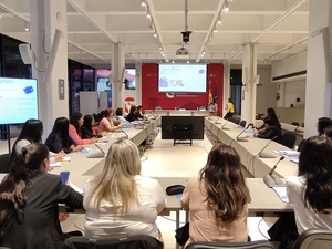 Una veintena de mujeres reunidas sentadas alrededor de una sala de juntas en escritorios