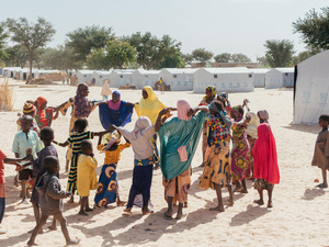 Un grupo de mujeres y niños refugiados juegan al corro en un campamento.