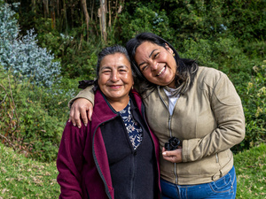 Dos mujeres sonríen a la cámara, al fondo un área verde