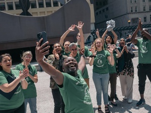 Un grupo de personas que visten camisetas verdes, levantan las manos