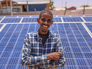 Un hombre somalí sonríe a la cámara; detrás suyo se ven paneles solares.
