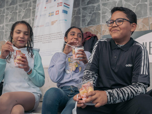 Dos niñas y un niño ríen mientras comen un postre en vasos transparentes de plástico