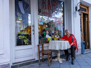 Una mujer de cabello corto que viste blusa roja y pantalón negro, sentada afuera de un restaurante.