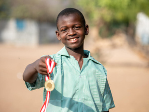 Un niño sonríe a la cámara mientras sostiene una medalla.