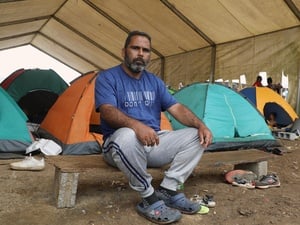 Un hombre sentado en un banco entre pequeñas carpas de acampar.