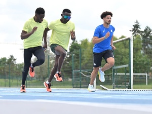 Tres atletas corren en paralelo en una pista azul