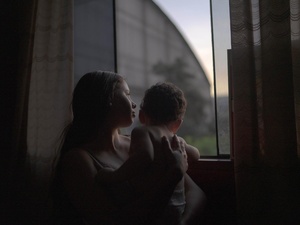 Yenifer está de pie con su hijo de 1 año junto a la ventana de la habitación en la que vive con su pareja a una hora de Lima, Perú. Llegaron a Perú en noviembre de 2019 desde Valencia, Venezuela.