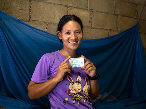 Una mujer con un documento de identidad en ambas manos sonríe a la cámara