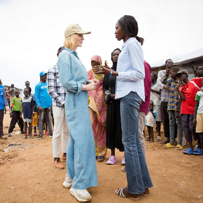 Una mujer caucásica charla con una mujer sudanesa; detrás de ellas, un numeroso grupo de personas.