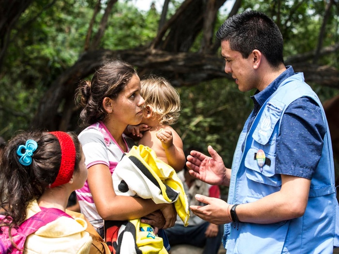 Una mujer con dos niños pequeños charla con un trabajador de ACNUR en Colombia.