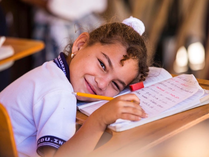 En una escuela en Colombia, una niña sonríe mientras se recuesta sobre su libreta en un aula.