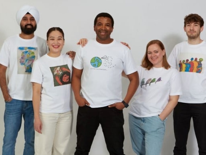 Cinco personas (tres hombres y dos mujeres), de nacionalidades distintas, sonríen a la cámara; cada una lleva puesta una de las camisetas del concurso de arte.