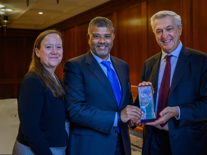 Una mujer y dos hombres posan para la foto, sosteniendo un pequeño certificado de cristal con el logotipo de ACNUR