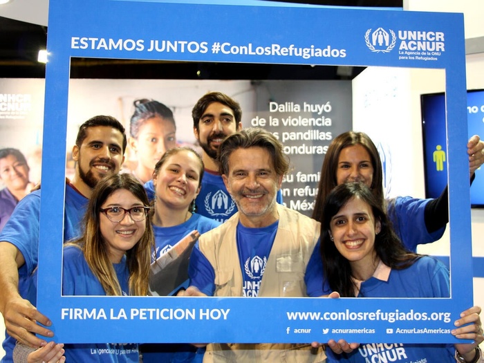 Un grupo de personas con la imagen de ACNUR sostiene un marco de fotos azul que dice "Estamos juntos #ConLosRefugiados" y "Firma la petición hoy"