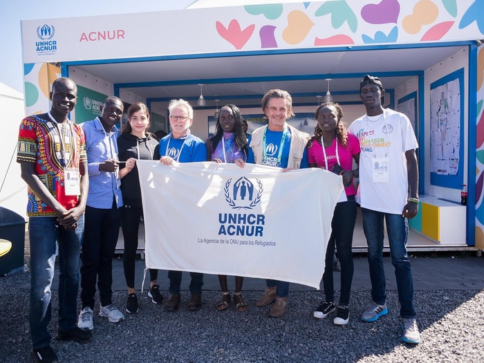 Un grupo de cinco hombres y tres mujeres sostienen una pancarta blanca con letras azules de ACNUR