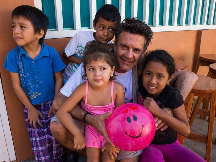 Un nombre junto a cuatro niños solicitantes de asilo, sostiene una pelota rosa con una carita sonriente.