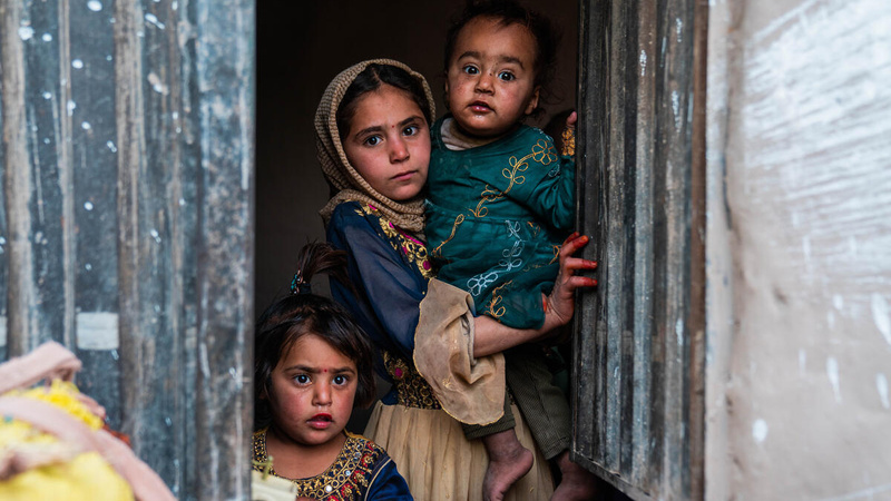 Dos niñas y un niño de distintas edades se asoman por una ventana; sus rostros muestran preocupación.