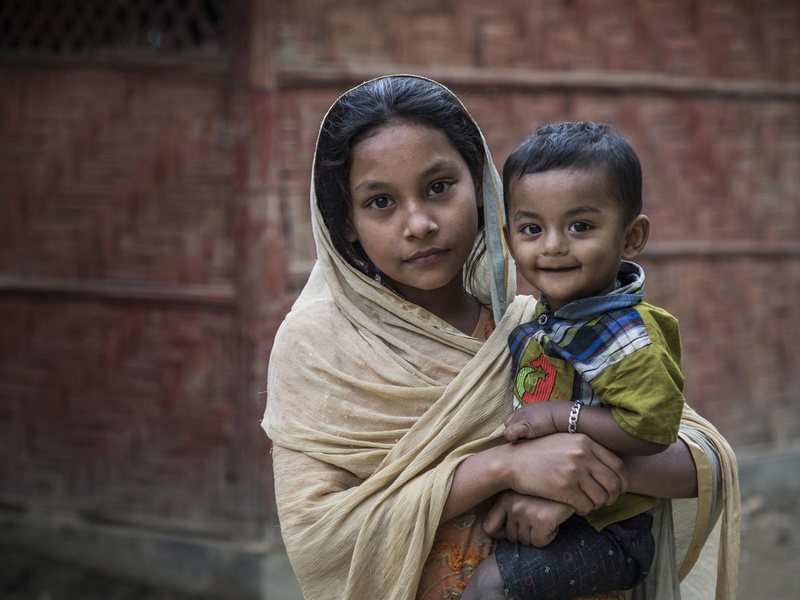 A young Rohingya girl holds her little brother