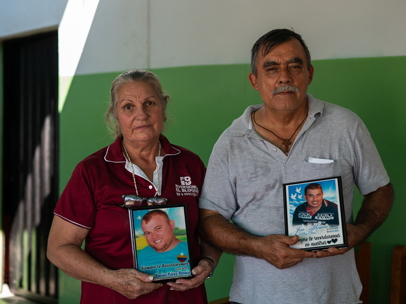 una mujer y un hombre mayores posan sujetando las fotos de dos hombres jóvenes.