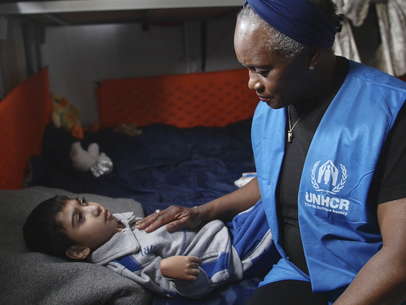 Una mujer afroestadunidense sentada junto a un niño que está postrado en una cama por la discapacidad con la que vive