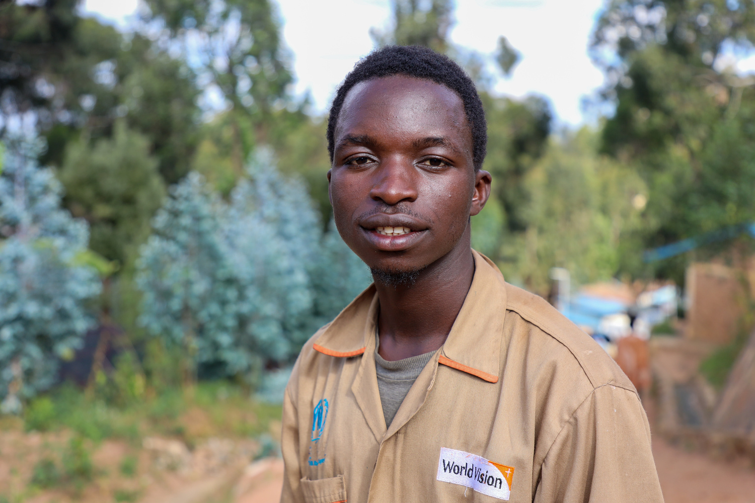 Un joven con camisa marrón en un vivero de árboles de un campamento de refugiados de Ruanda.