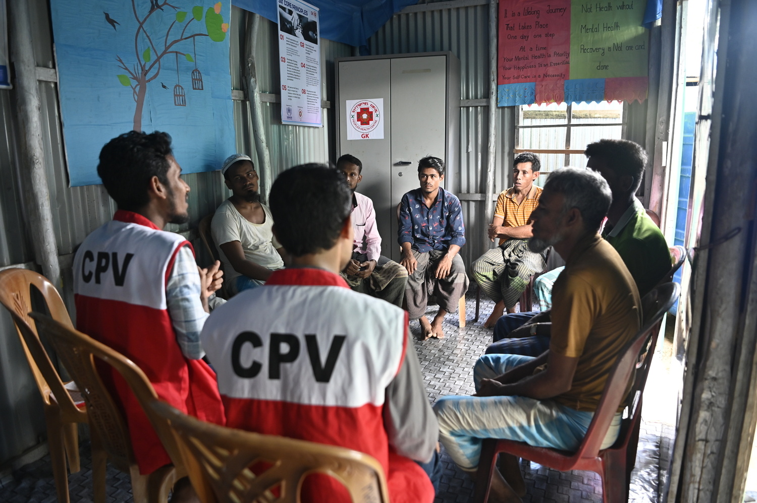 Dos hombres voluntarios dirigen una sesión de apoyo a un grupo de seis hombres refugiados rohingyas sobre crianza positiva