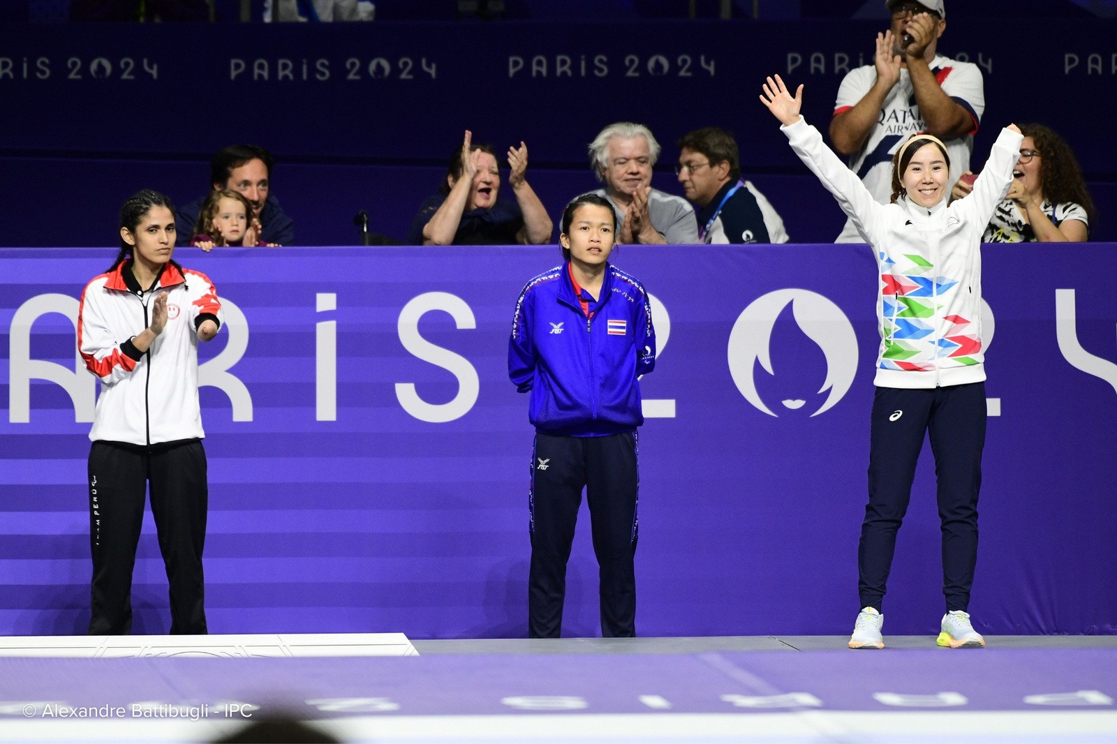 Una atleta levanta los brazos en señal de celebración mientras otras dos celebran con la mirada