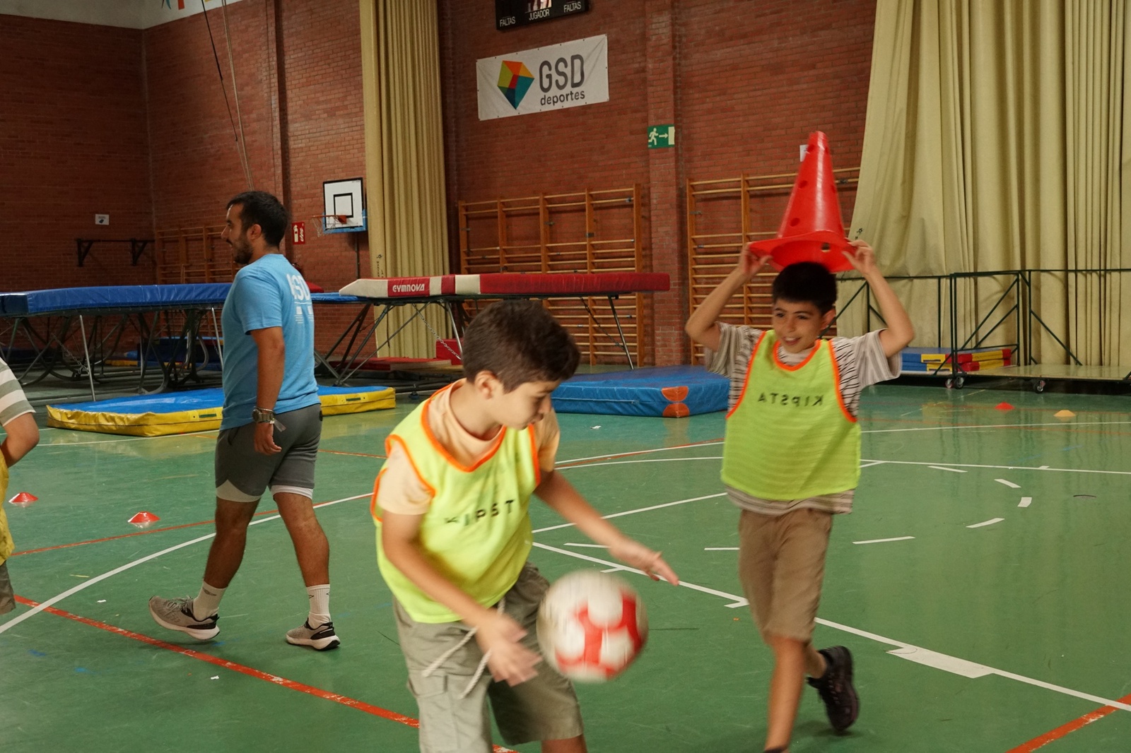 Dos niños juegan a una carrera de relevos con un cono en el polideportivo de GSD Vallecas.