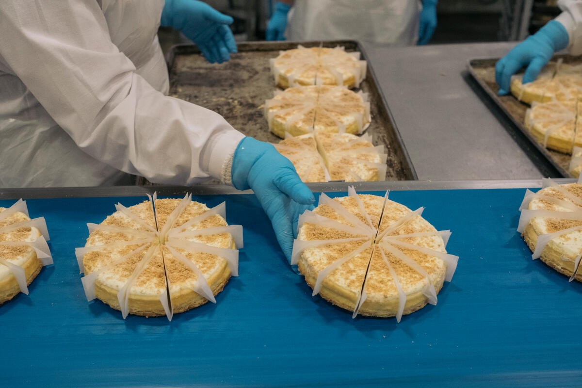 Un trabajador de una fábrica coloca una tarta de queso en una cinta transportadora.