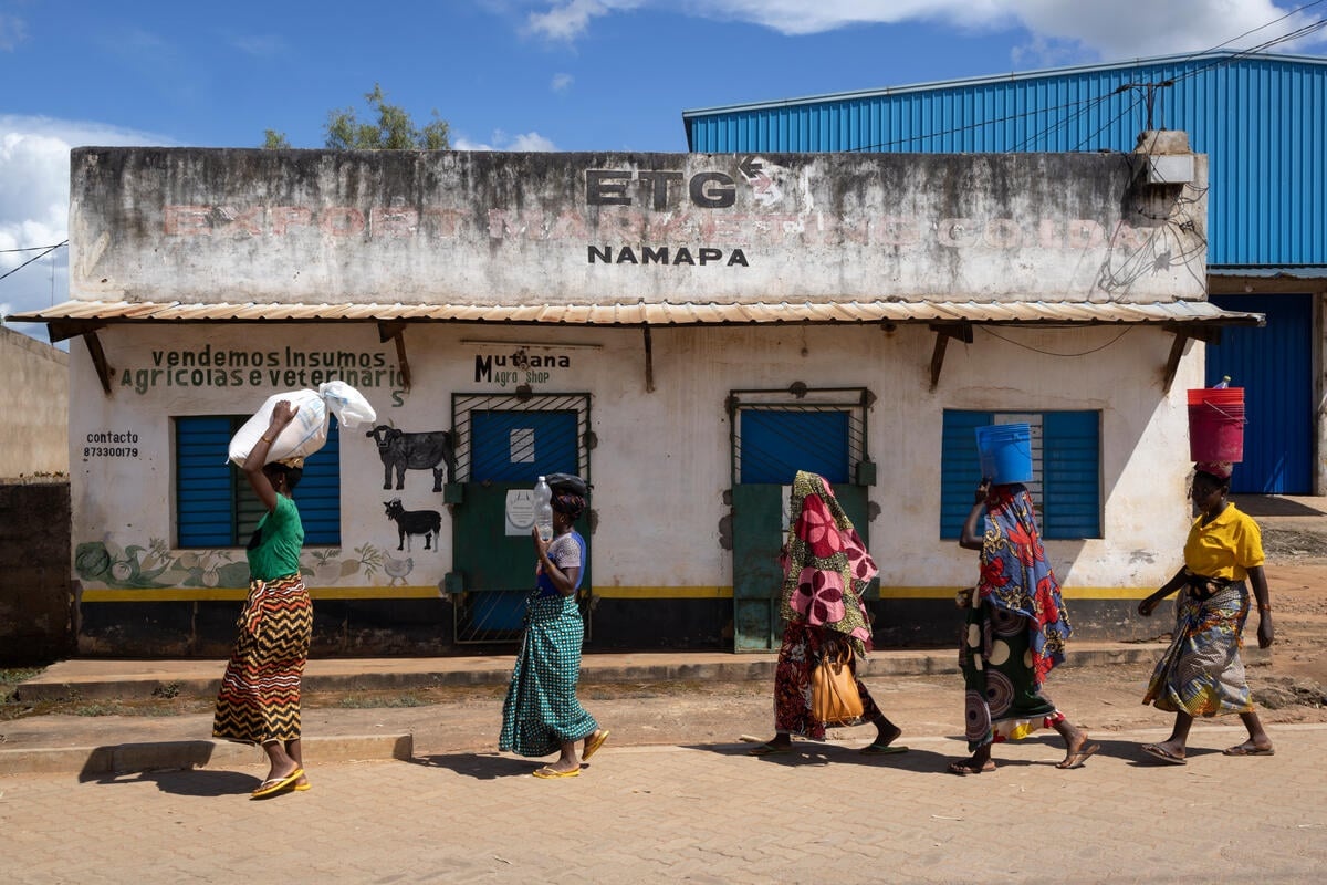 Cinco mujeres que viste faldas de colores caminan en fila con artículos sobre sus cabezas