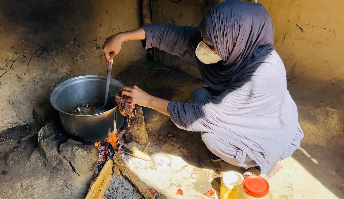 Una mujer sentada en el suelo prepara comida en un fogón