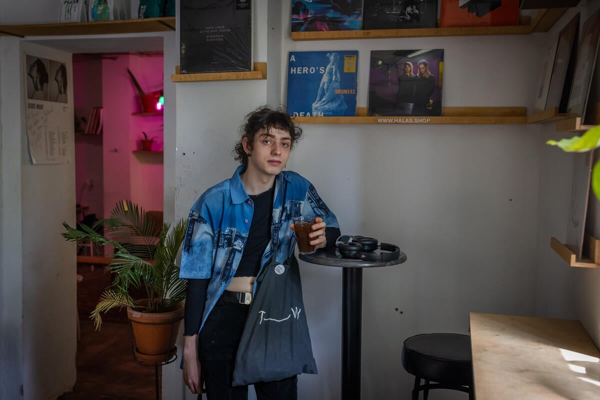 Una mujer que viste camisa azul está recargada sobre una mesa negra de un café