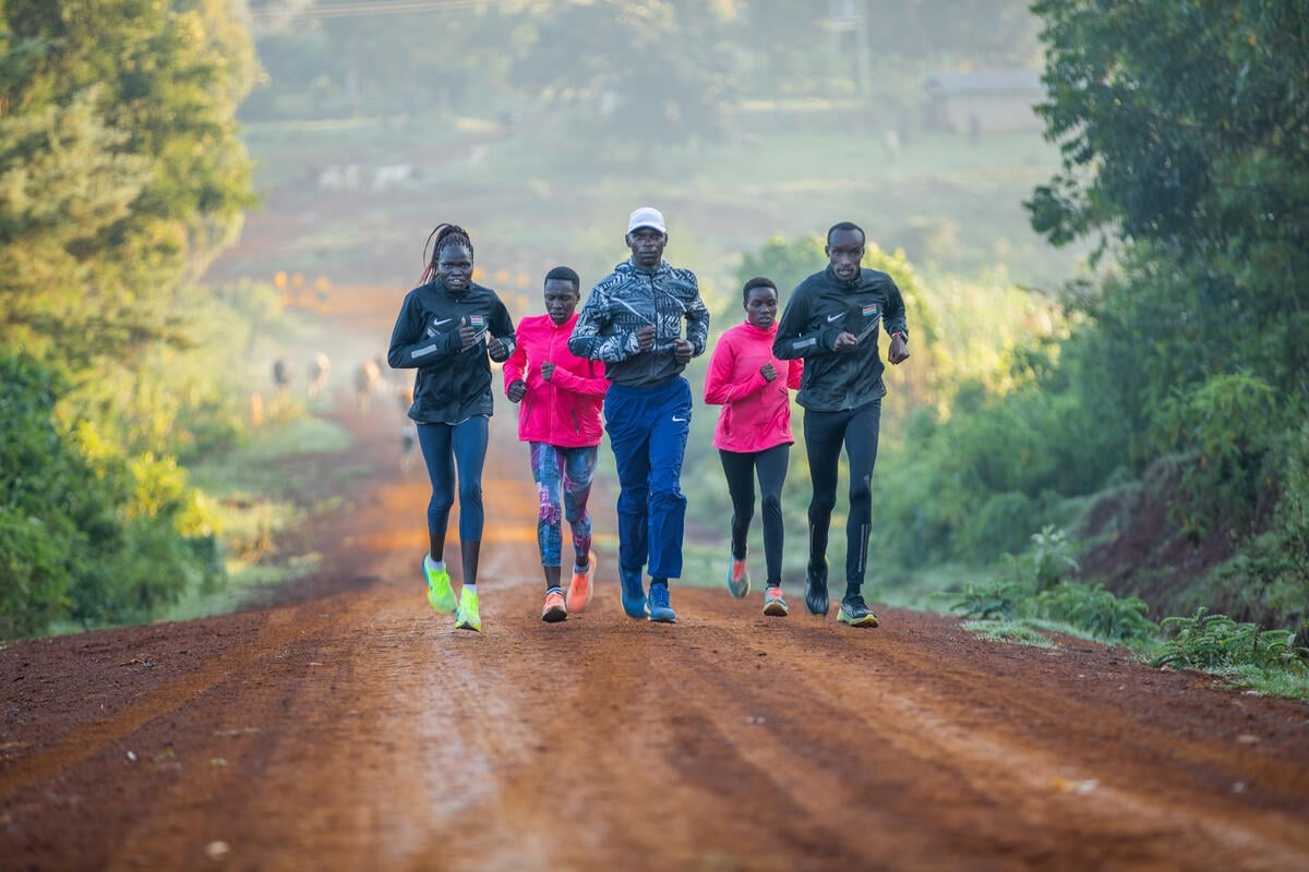Un grupo de cinco personas (tres mujeres y dos hombres) corre por un camino de tierra rodeado de árboles