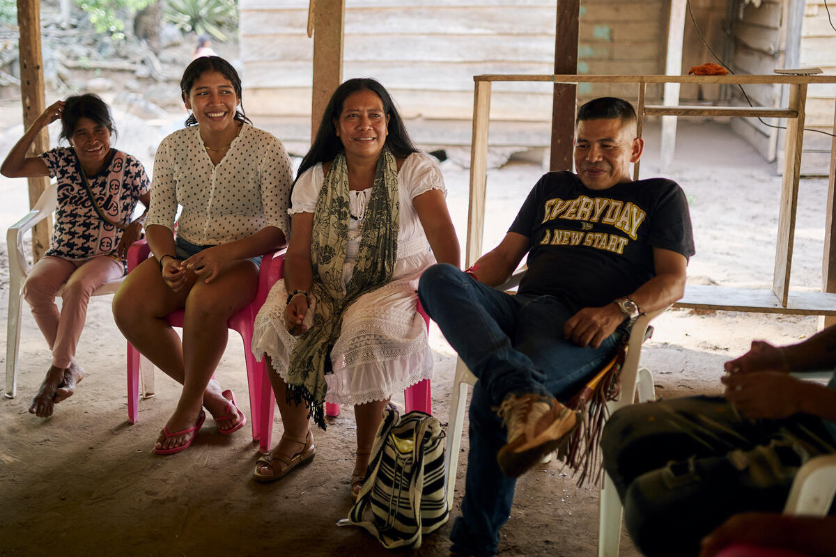 Un hombre y tres mujeres sentados en sillas de plástico bajo un albergue al aire libre
