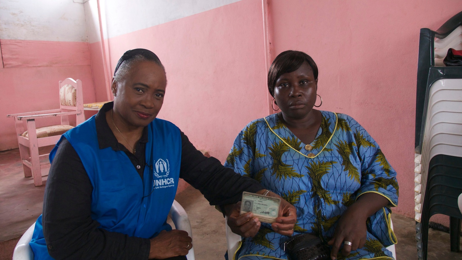 Dos mujeres afro sentadas una a lado de la otra; una de ellas muestra su documento de identidad.